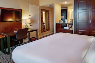 A hotel room with a large bed, a desk with a chair, a television, a mirror, and a wardrobe.