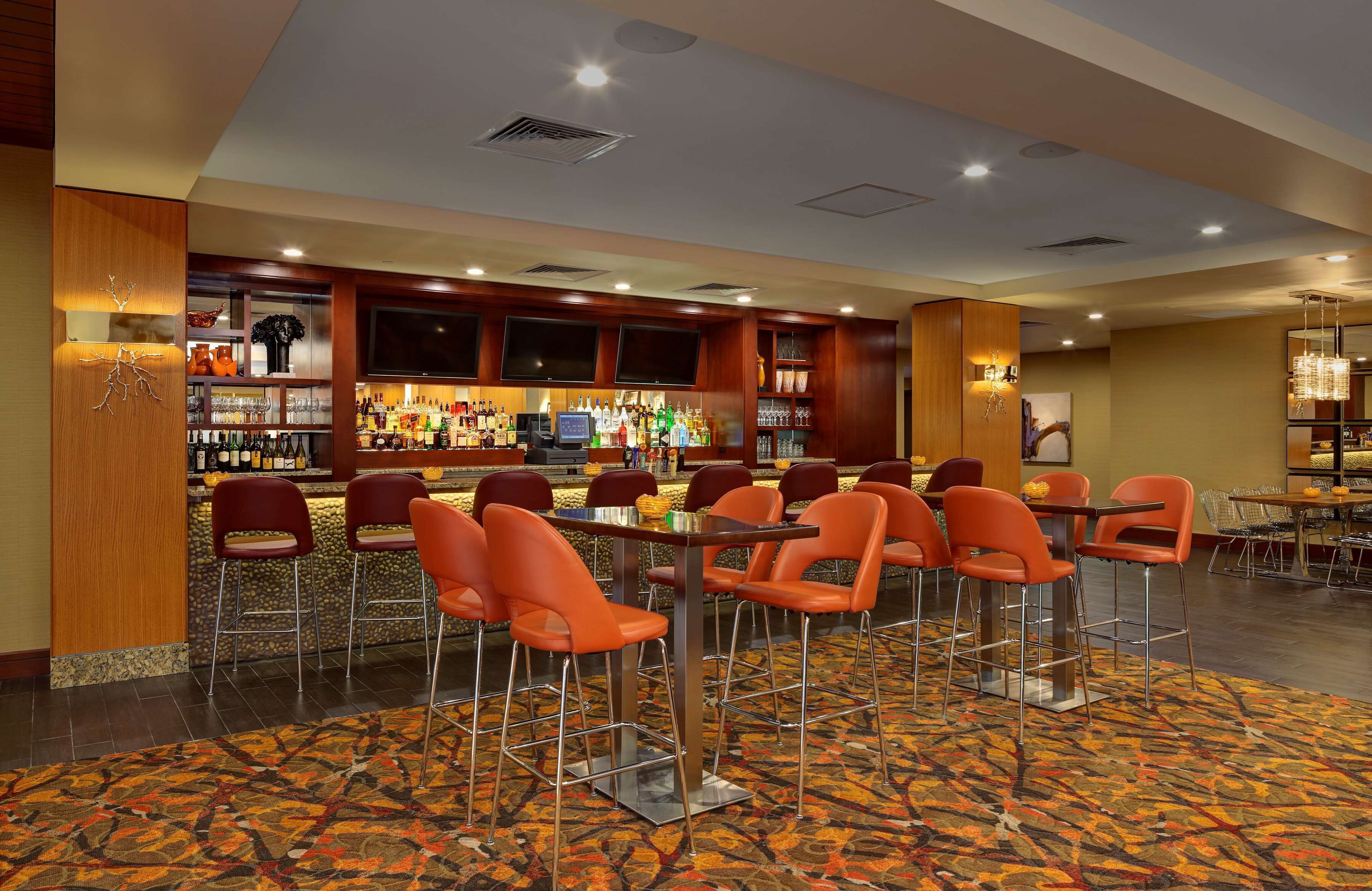A bar area with multiple seating options, including bar stools and tables, and a variety of bottles and glasses on shelves.