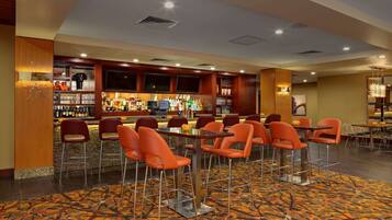A bar area with multiple seating options, including bar stools and tables, and a variety of bottles and glasses on shelves.