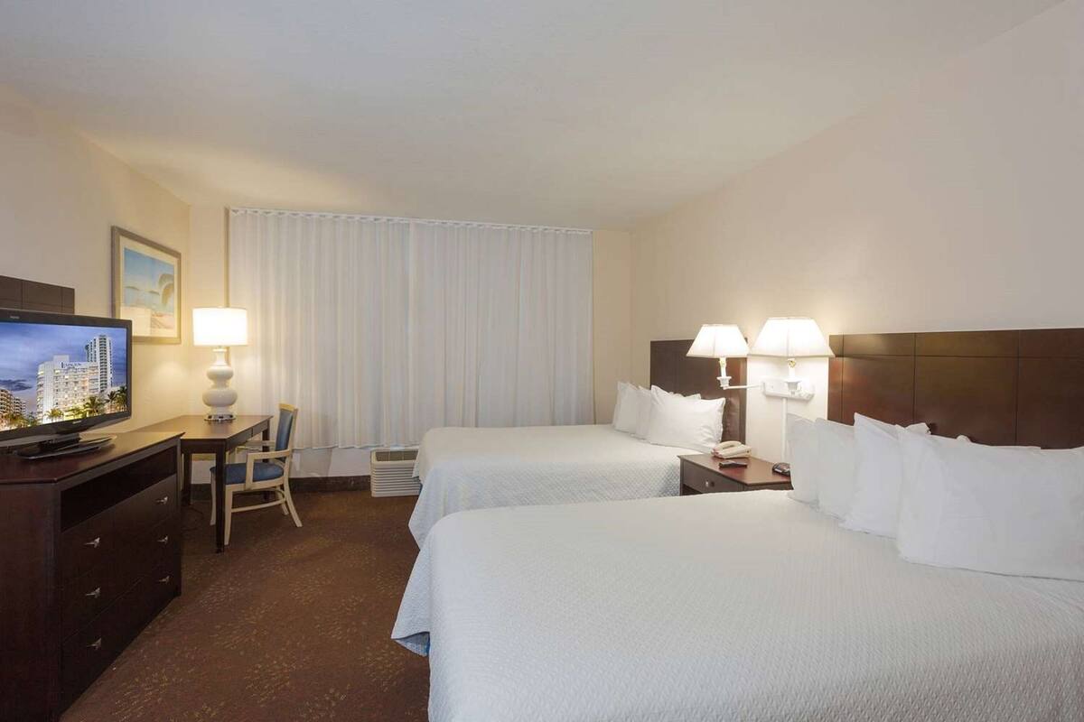 A hotel room with two beds, a TV, a desk, and a chair.