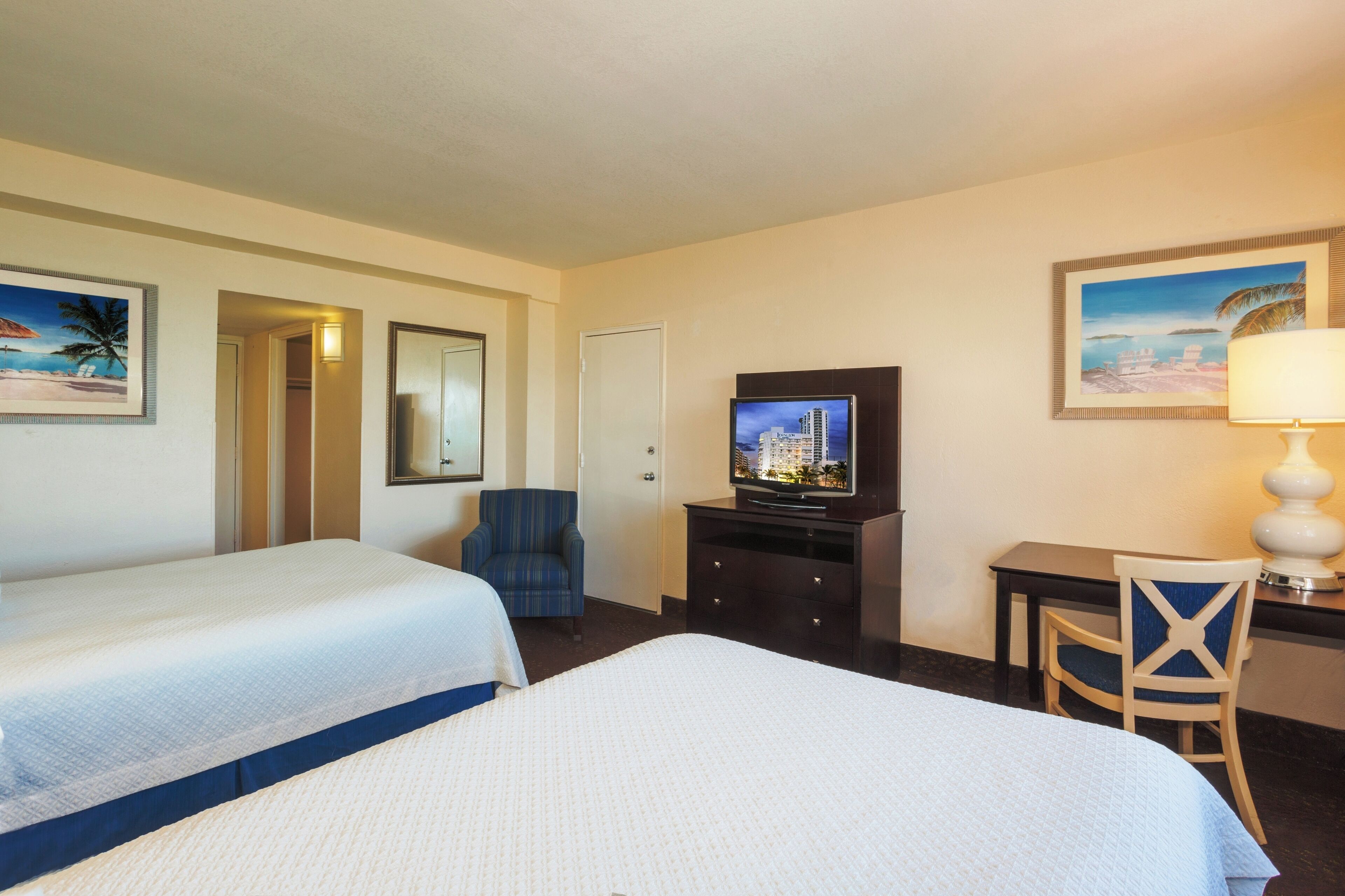 A hotel room with two beds, a desk, a television, and a lamp.