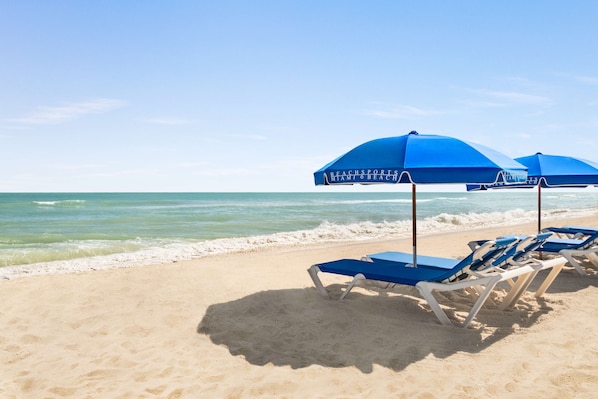 Na praia, espreguiçadeiras, guarda-sóis, toalhas de praia 