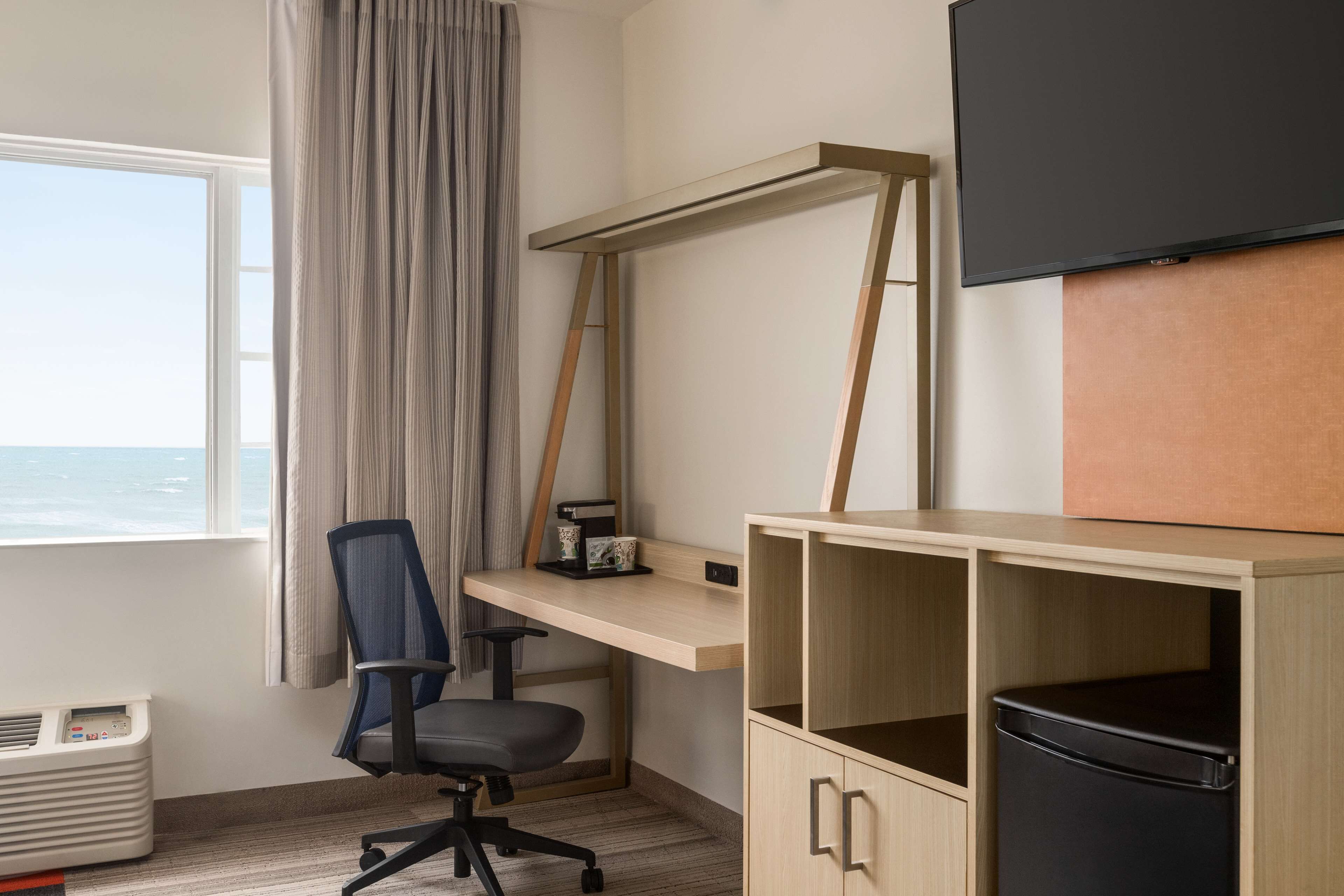 A room with a desk, chair, and a TV mounted on the wall.