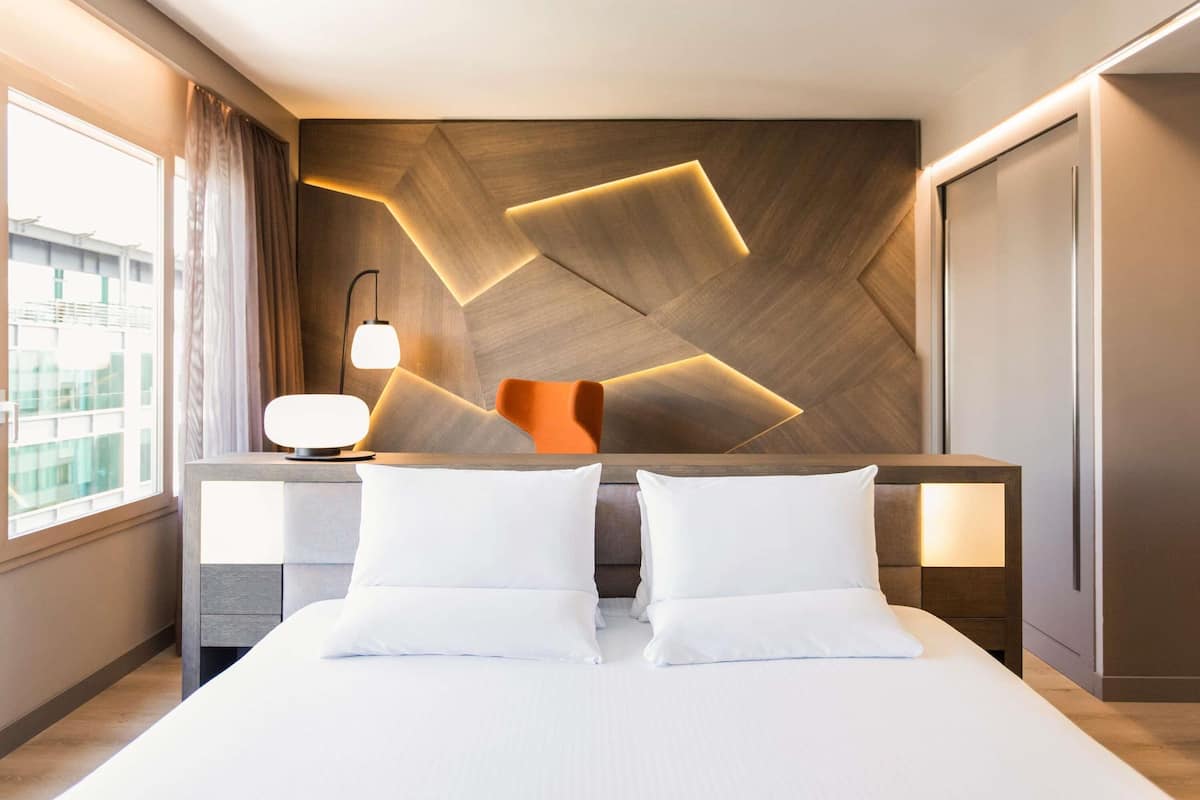 Et moderne hotelværelse med en stor seng, to sengeborde, et natbord og en væg med geometrisk mønster.