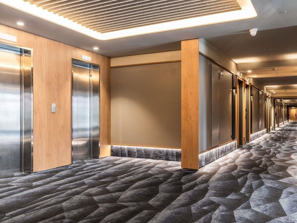 A hotel hallway with elevators, wooden paneling, and a patterned carpet.
