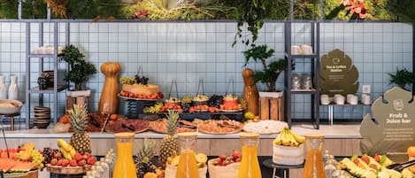 A buffet with a variety of food and drinks, including fruits, cheeses, and pastries.