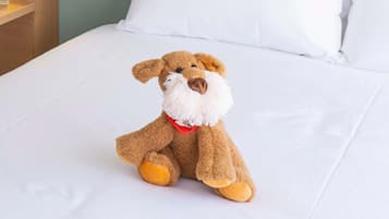 Un peluche sobre una cama con ropa de cama blanca.
