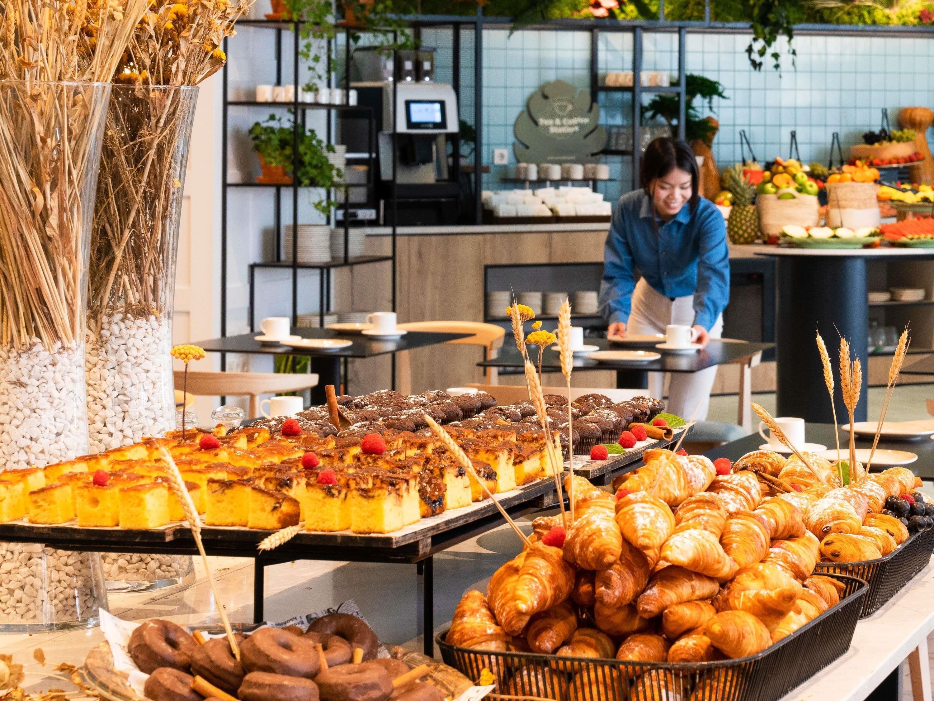 A buffet with pastries, a coffee machine, and a person serving food.