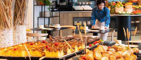 A buffet with pastries, a coffee machine, and a person serving food.