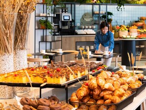 A buffet with pastries, a coffee machine, and a person serving food. - Novotel Madrid Feria and Airport (Madrid)