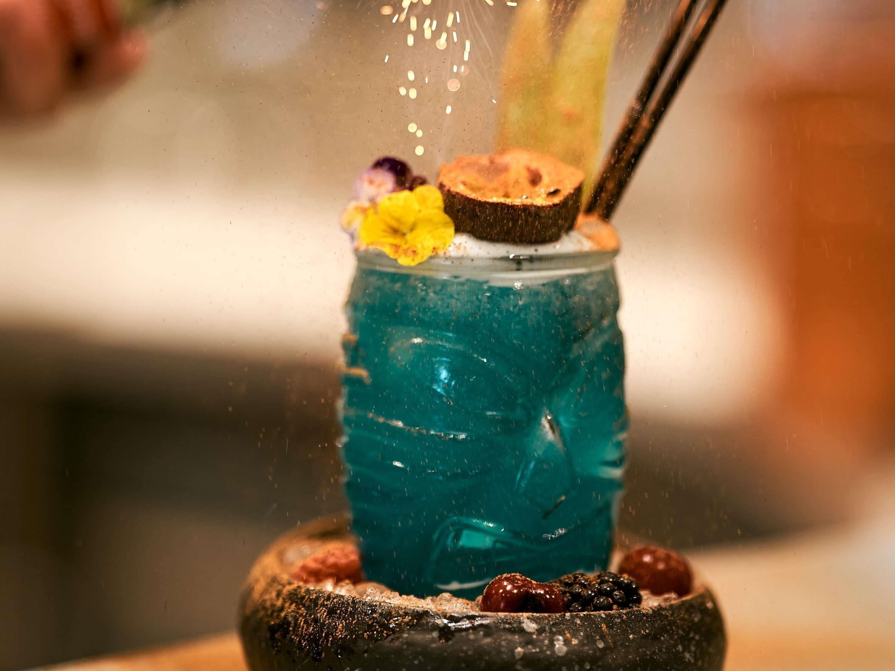 Un cocktail agrémenté d’une fleur et servi avec une paille, dans un verre au décor texturé.