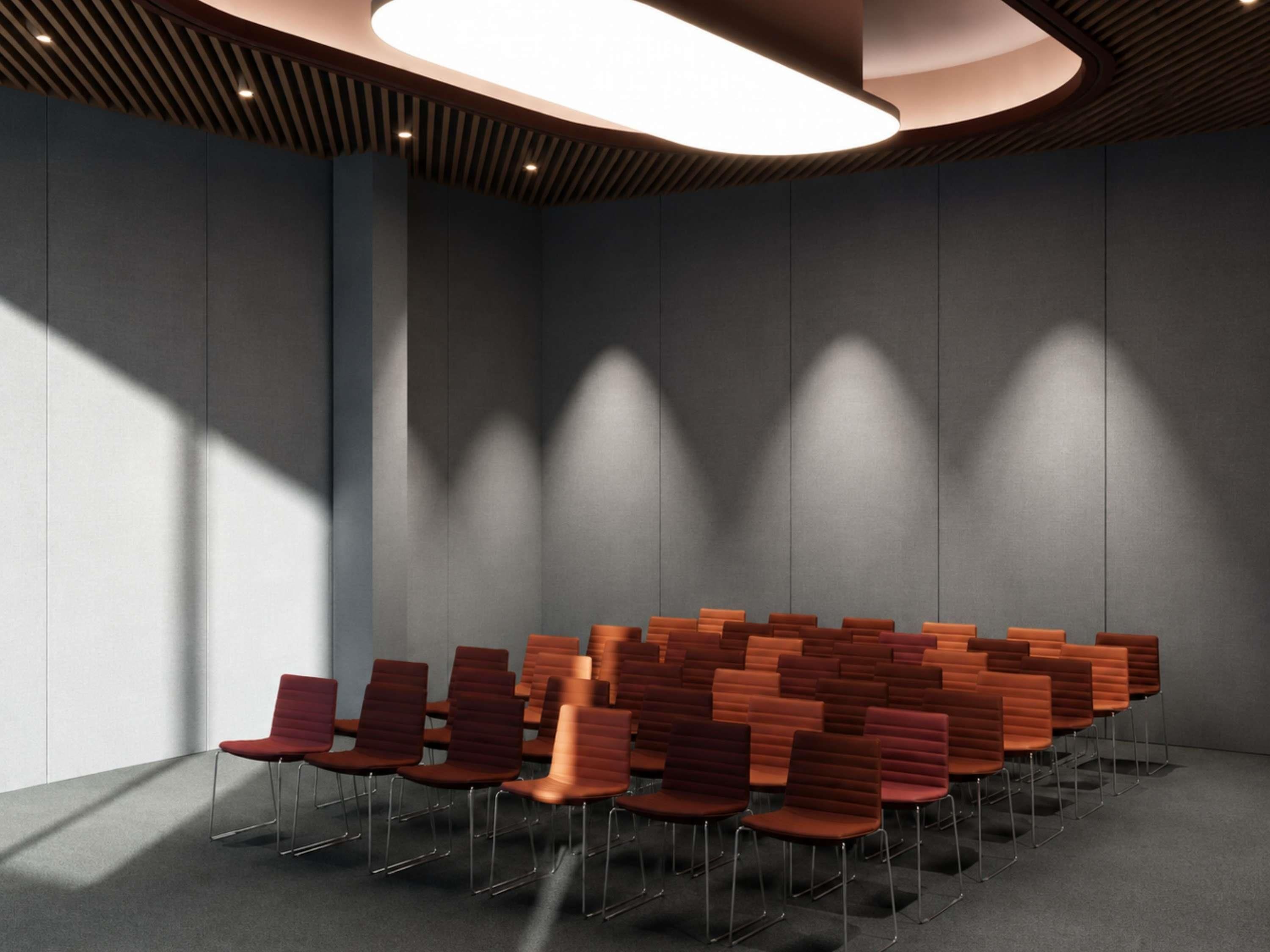 Un salón de conferencias con filas de sillas, una lámpara de techo moderna y una pared lisa.
