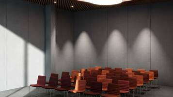 Un salón de conferencias con filas de sillas, una lámpara de techo moderna y una pared lisa.