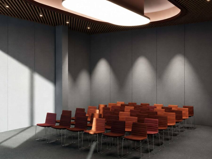 Un salón de conferencias con filas de sillas, una lámpara de techo moderna y una pared lisa.