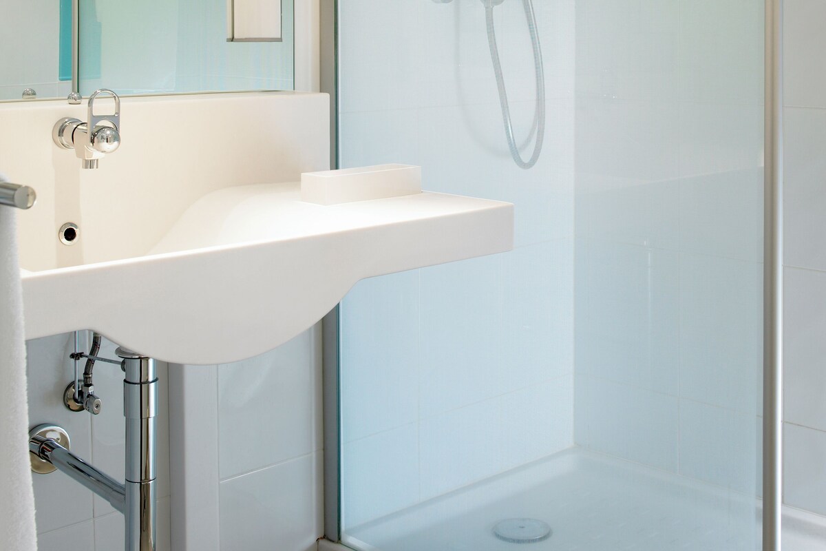 A modern bathroom with a glass shower enclosure, a white sink, and a mirror.