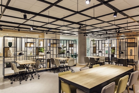 A modern conference room with multiple tables and chairs, featuring a grid ceiling with exposed beams and pendant lighting.