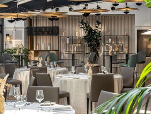 Un restaurant avec des tables rondes, des chaises grises et des luminaires suspendus.