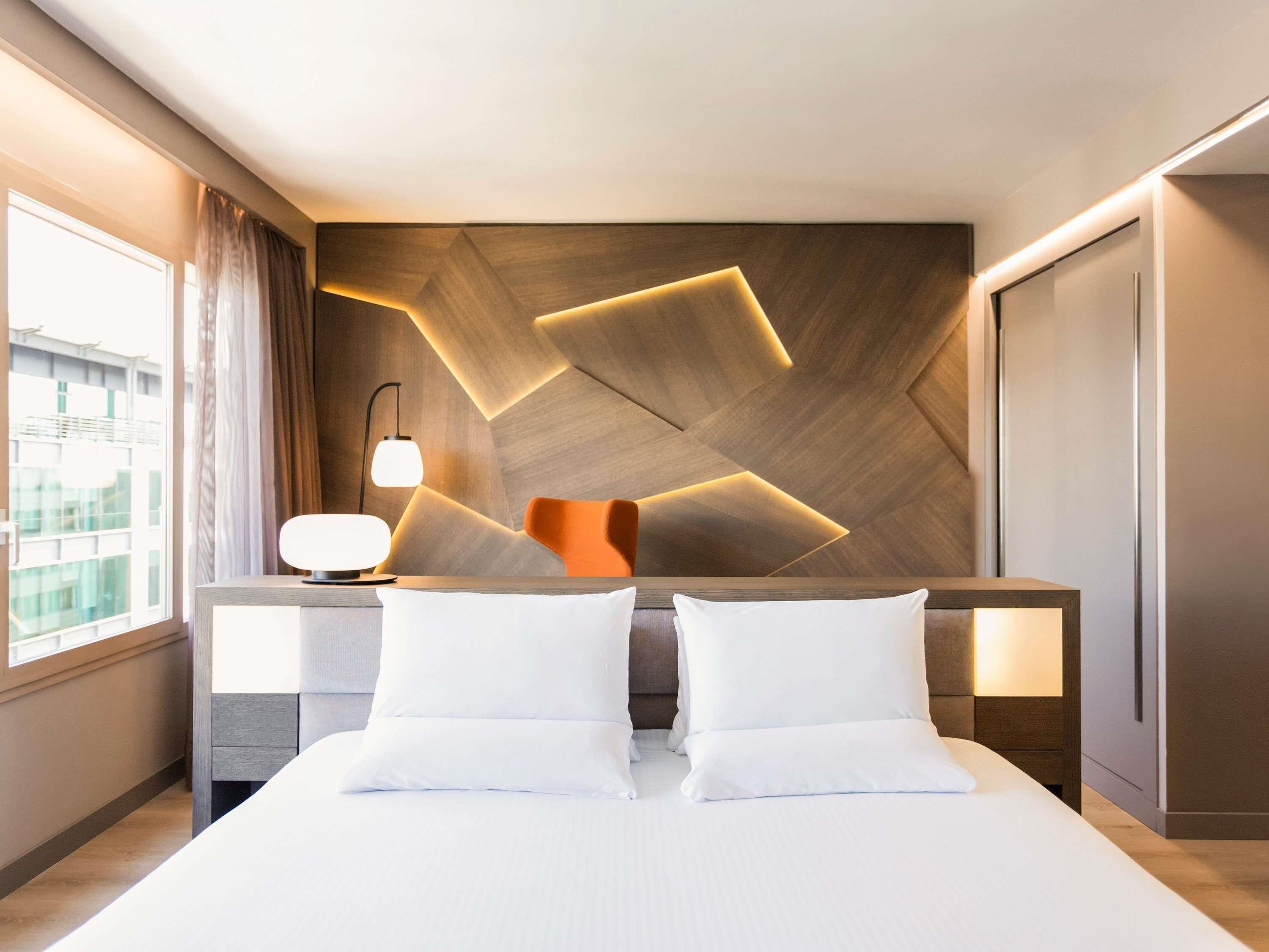 Een moderne hotelkamer met een groot bed, twee nachtkastjes en een muur met een geometrisch patroon.