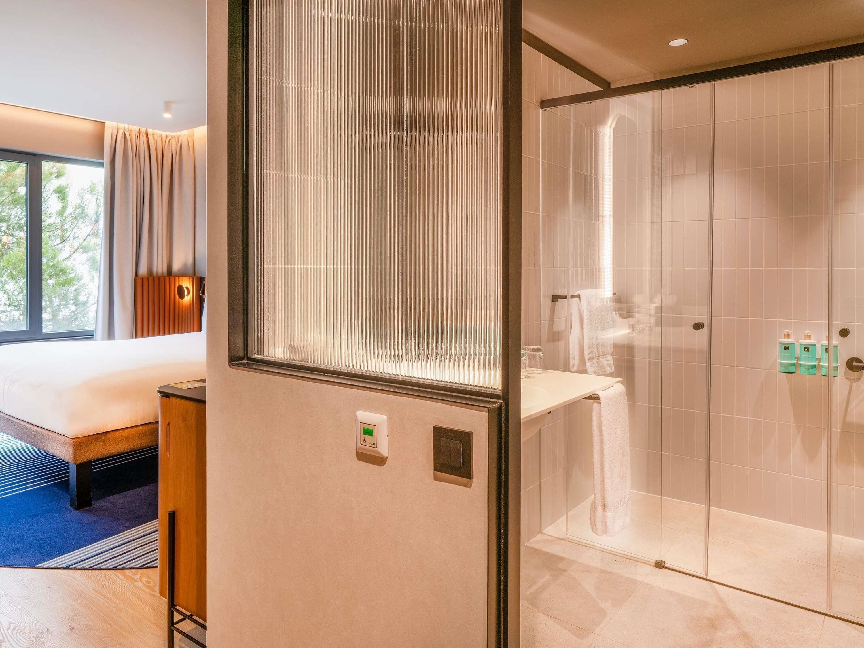 Une chambre d’hôtel avec un lit, une salle de bain avec une douche en verre et une fenêtre avec des rideaux.