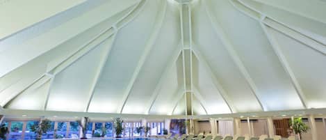 An indoor swimming pool with a high, white, geometric ceiling and lounge chairs along the poolside.