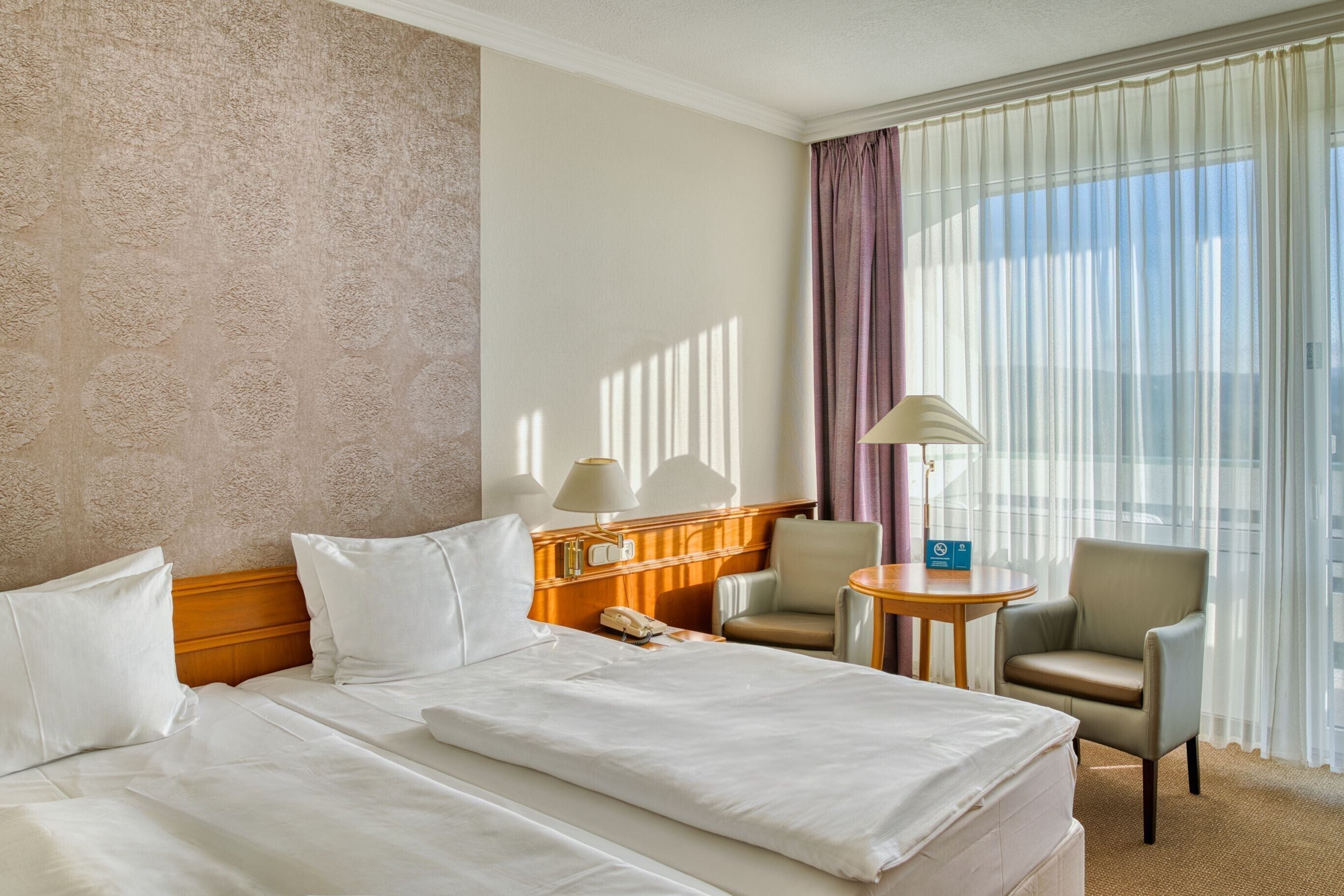 A hotel room with a large bed, two chairs, a small table, and a lamp.