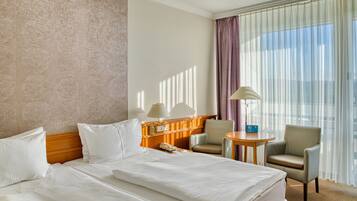 A hotel room with a large bed, two chairs, a small table, and a lamp.