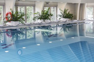 Una piscina interior con paredes de vidrio transparente, plantas en macetas y un flotador.
