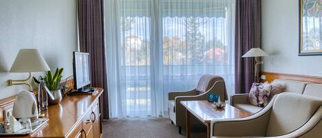 Una habitación de hotel con un escritorio de madera, televisor, sofá y ventana con cortinas.