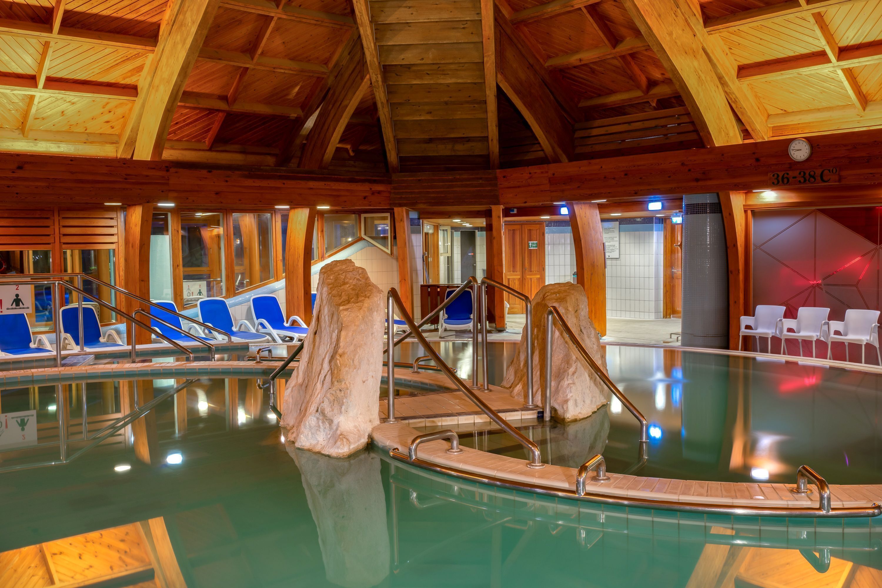 An indoor swimming pool with wooden beams, blue chairs, and a wooden boat structure.