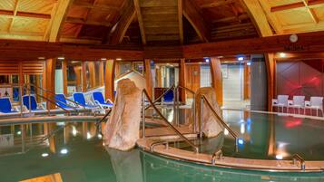 An indoor swimming pool with wooden beams, blue chairs, and a wooden boat structure.