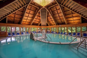 An indoor swimming pool with a wooden roof structure, clear blue water, and blue lounge chairs around the perimeter. - Ensana Thermal Hévíz (Hévíz)