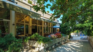 Un restaurante con terraza, grandes ventanales y un jardín con plantas y flores.
