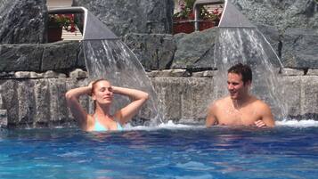 A swimming pool with water jets and a stone wall in the background.