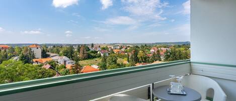 A balcony with a table and chairs, overlooking a residential area with houses and trees.