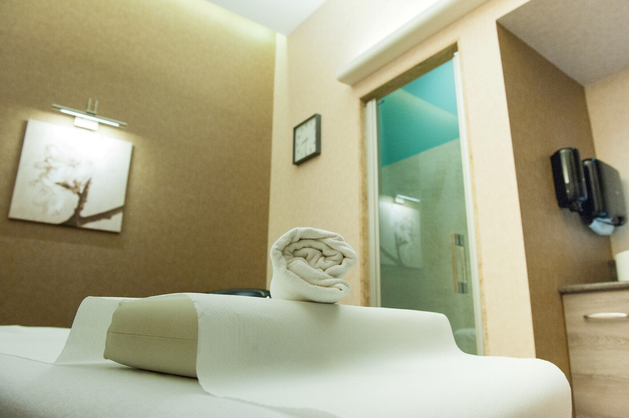 Une chambre d’hôtel avec un lit, une serviette, une horloge et un téléphone fixé au mur.
