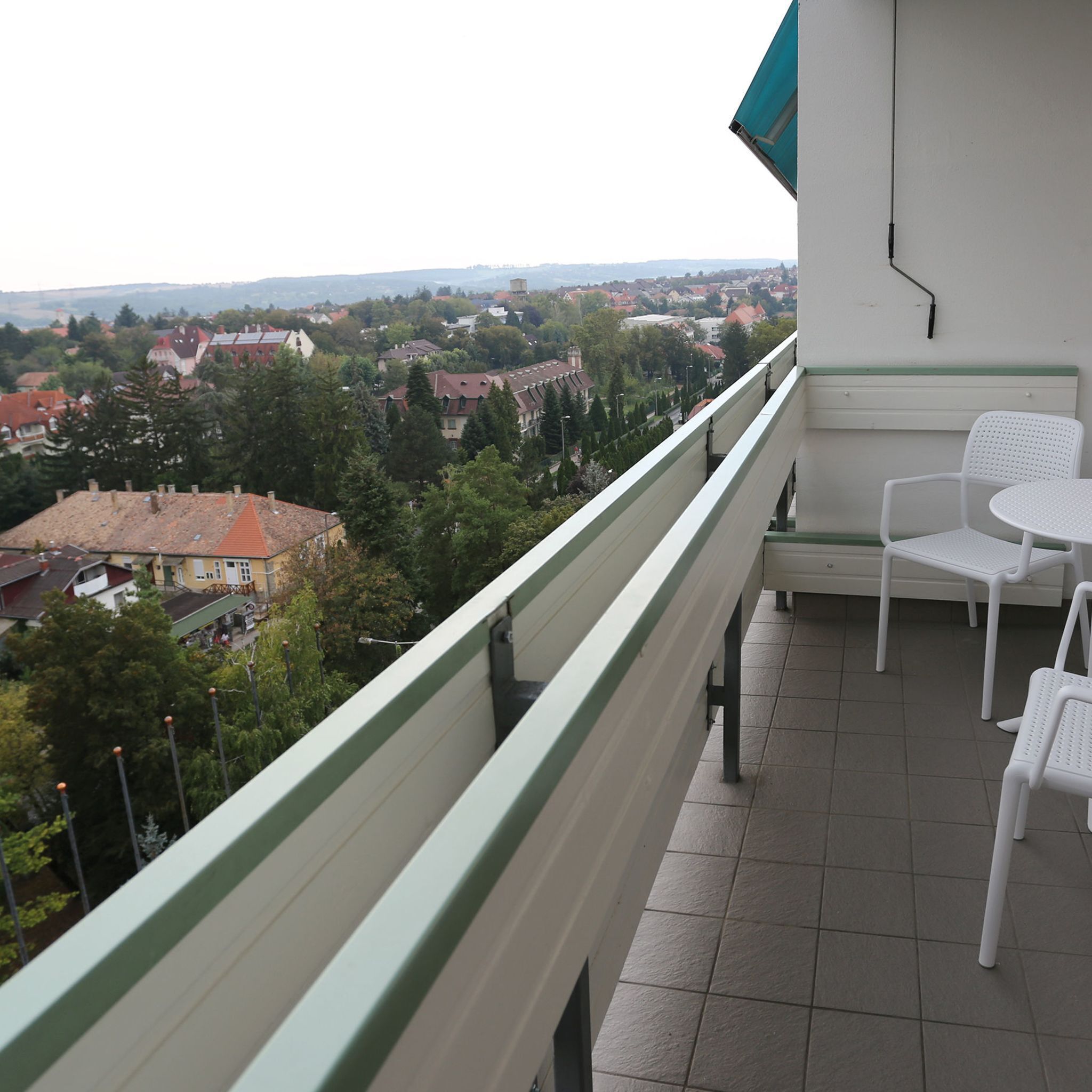 Un balcón con vistas a un pueblo, sillas blancas y una mesa.