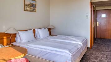 A hotel room with a bed, two bedside tables, a lamp, a painting on the wall, and a door.