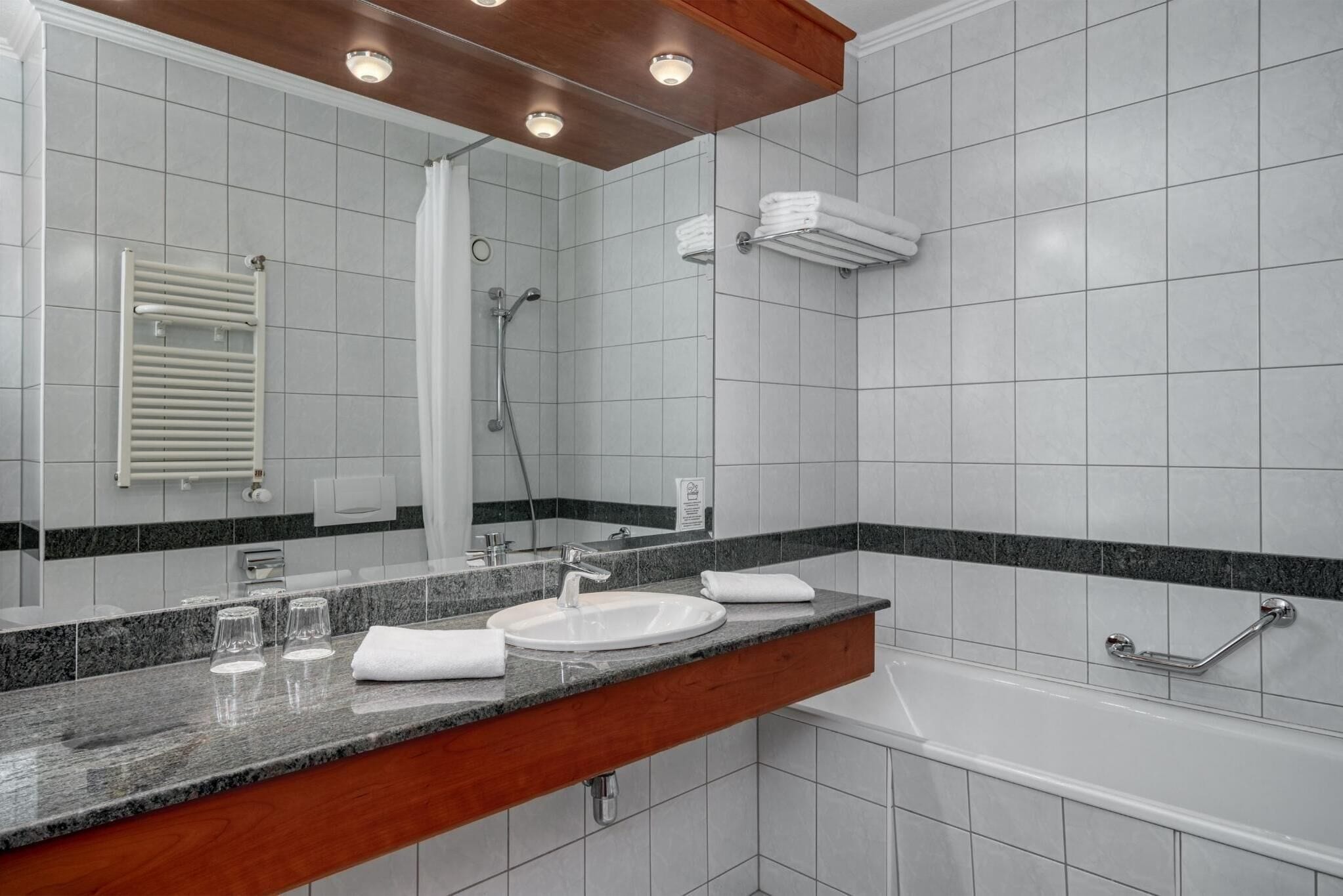 A modern bathroom with a granite countertop, a white sink, a mirror, a shower, and a bathtub.