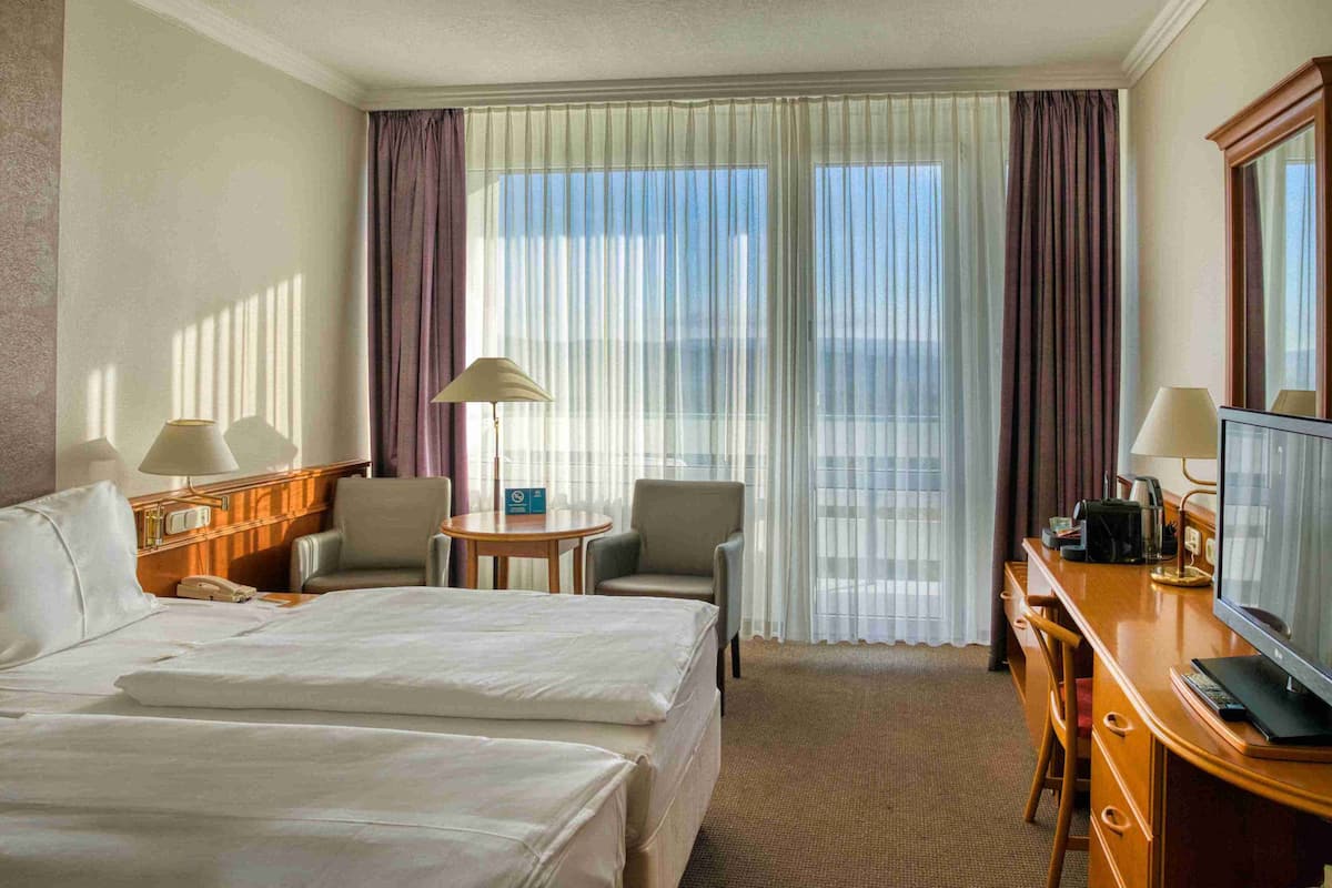 A hotel room with two beds, a desk, a chair, a TV, and a window with curtains.