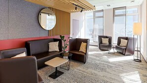 A modern lobby with a sofa, chairs, a small table, a mirror, and a lamp.