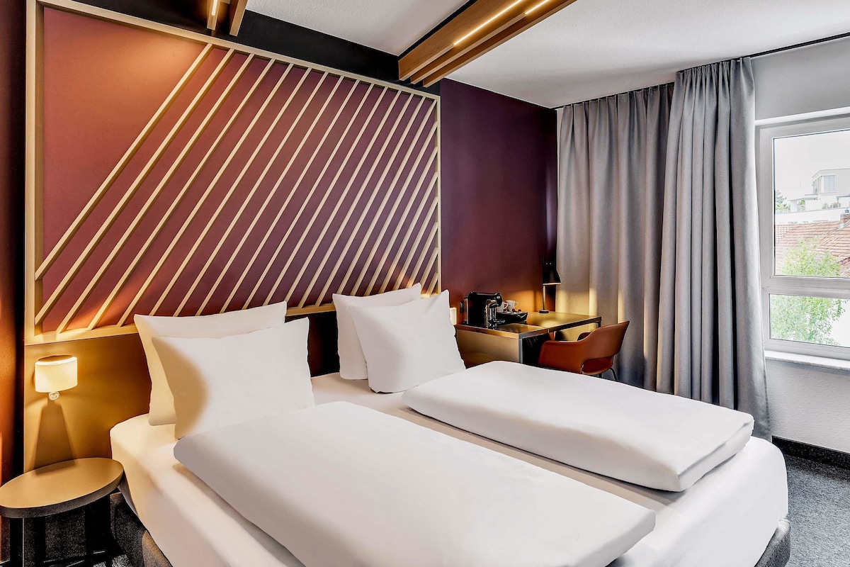 Una habitación de hotel con una cama grande, un escritorio, una lámpara y vistas al exterior.