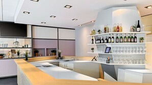 A modern bar area with a wooden counter, shelves with bottles and glasses, and a large window with decorative items.
