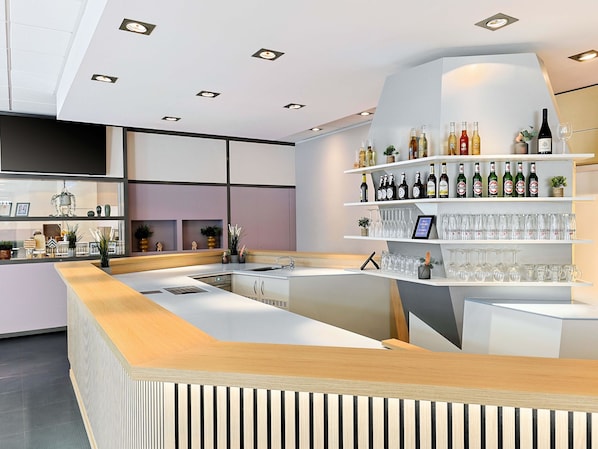 Un espace bar moderne avec un comptoir en bois, des étagères remplies de bouteilles et de verres, et une grande fenêtre agrémentée d’objets décoratifs.