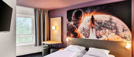 Habitación de hotel con dos camas, un mural grande de una escena espacial, una ventana con cortinas y una mesita pequeña.