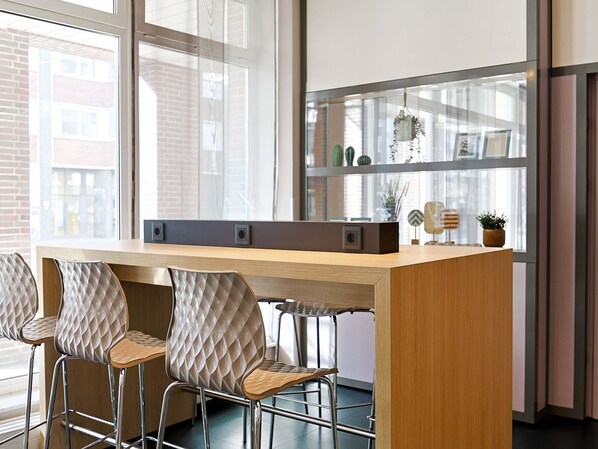 A modern office space with a long wooden desk, three cushioned chairs, and a large window with a view of buildings. - B&B Hotel Bremen-Altstadt (Bremen)