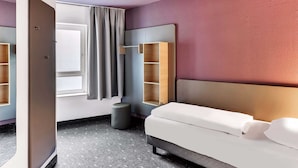 A modern hotel room with a grey sofa, a large mirror, a wardrobe, and a small stool.