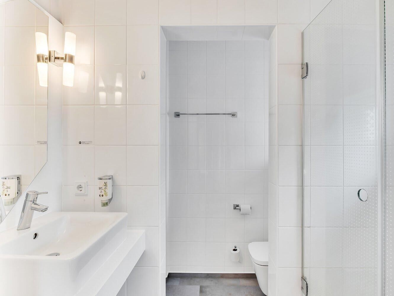Un baño moderno con lavamanos blanco, espejo y zona de ducha.