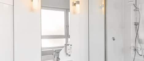 A modern bathroom with a glass-enclosed shower, a white sink, and two wall-mounted lights.