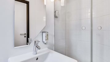 Un baño moderno con un lavabo blanco, un espejo y una cabina de ducha de vidrio.