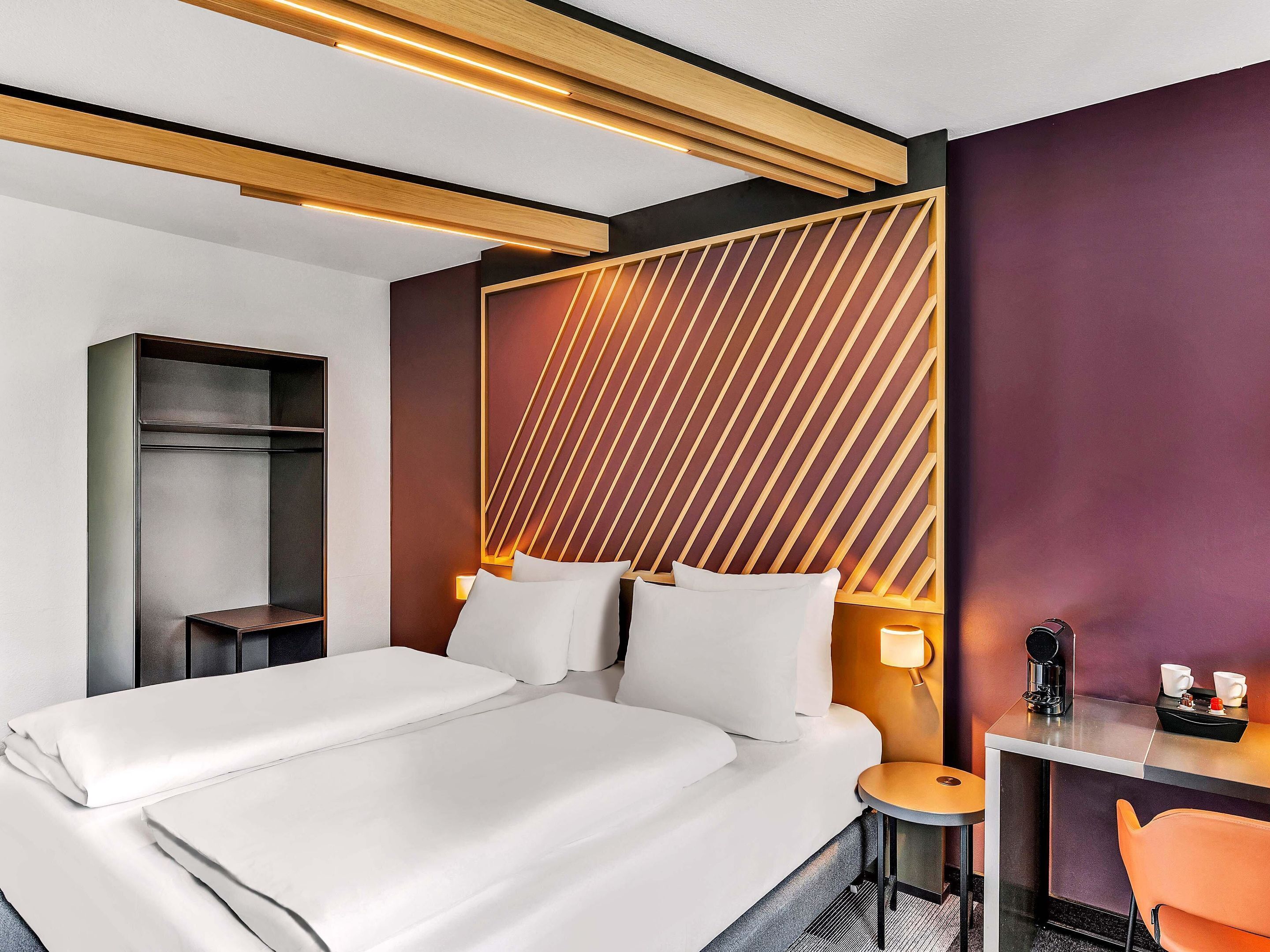 Una habitación de hotel moderna con una cama grande, mesitas de noche, un escritorio y una silla.